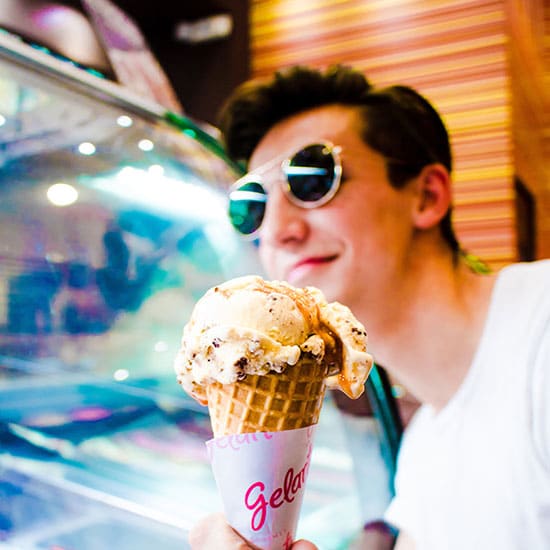 man with sunglasses on, holding up waffle cone filled with ice cream