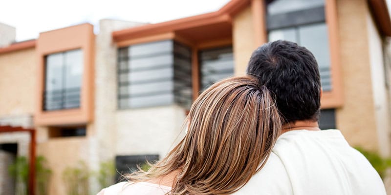 hugging couple looking up at their new home exterior