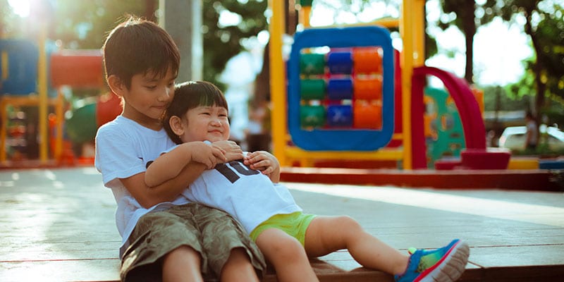 siblings playing together with playground in the background