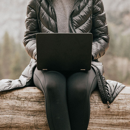 single individual sitting on a log in the mountains, checking their laptop