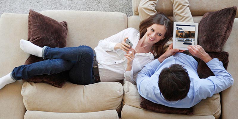 couple relaxing together on their couch with smartphone and tablet