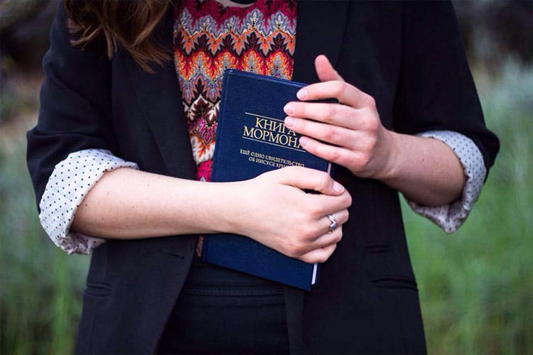 Sister missionary holding a copy of the Book of Mormon in a foreign language
