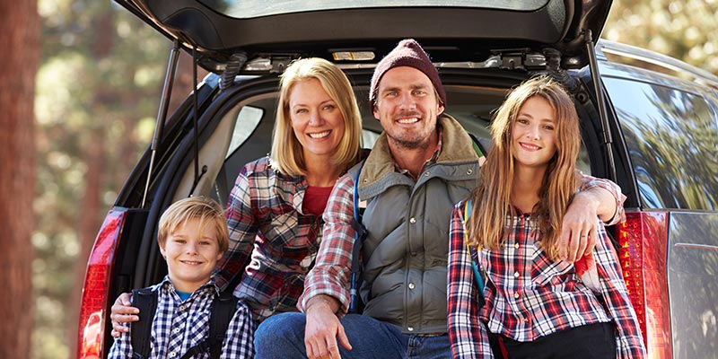 smiling family in the back of their car, camping in the woods