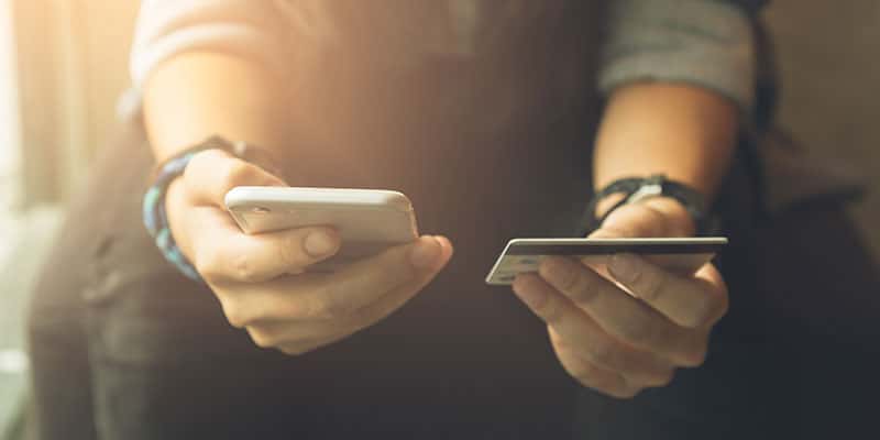 young person making mobile transaction, phone and credit card in hands