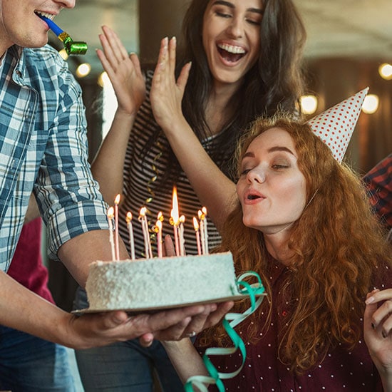 young adult friends celebrating a birthday together, blowing out candles on a cake