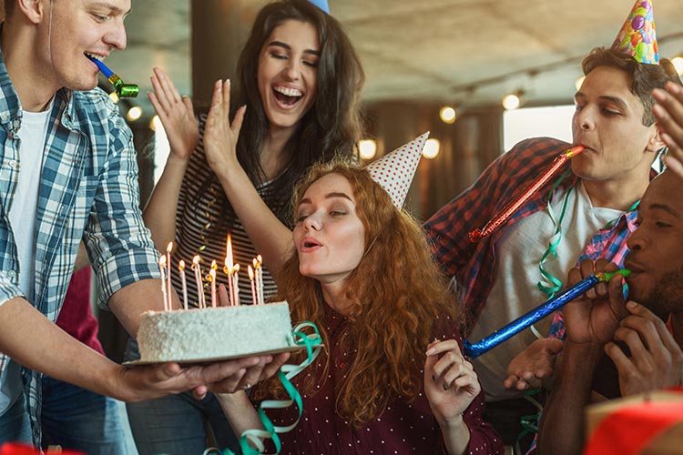 young adult friends celebrating a birthday together, blowing out candles on a cake