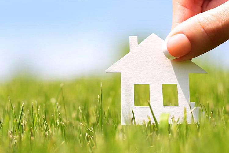 close up of a paper house cutout, fingers holding it in the grass