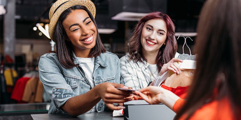 happy women out shopping together, handing card to cashier