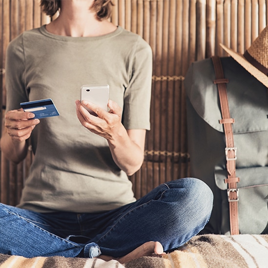 Woman sitting on a bed holding a phone and credit card