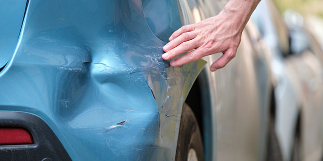 Hand touching the broken rear bumper of a car