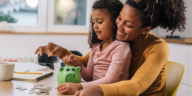 Mother and daughter placing coins in a piggy bank.
