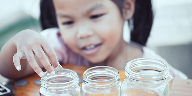 Young girl placing a coin in one of three mason jars.
